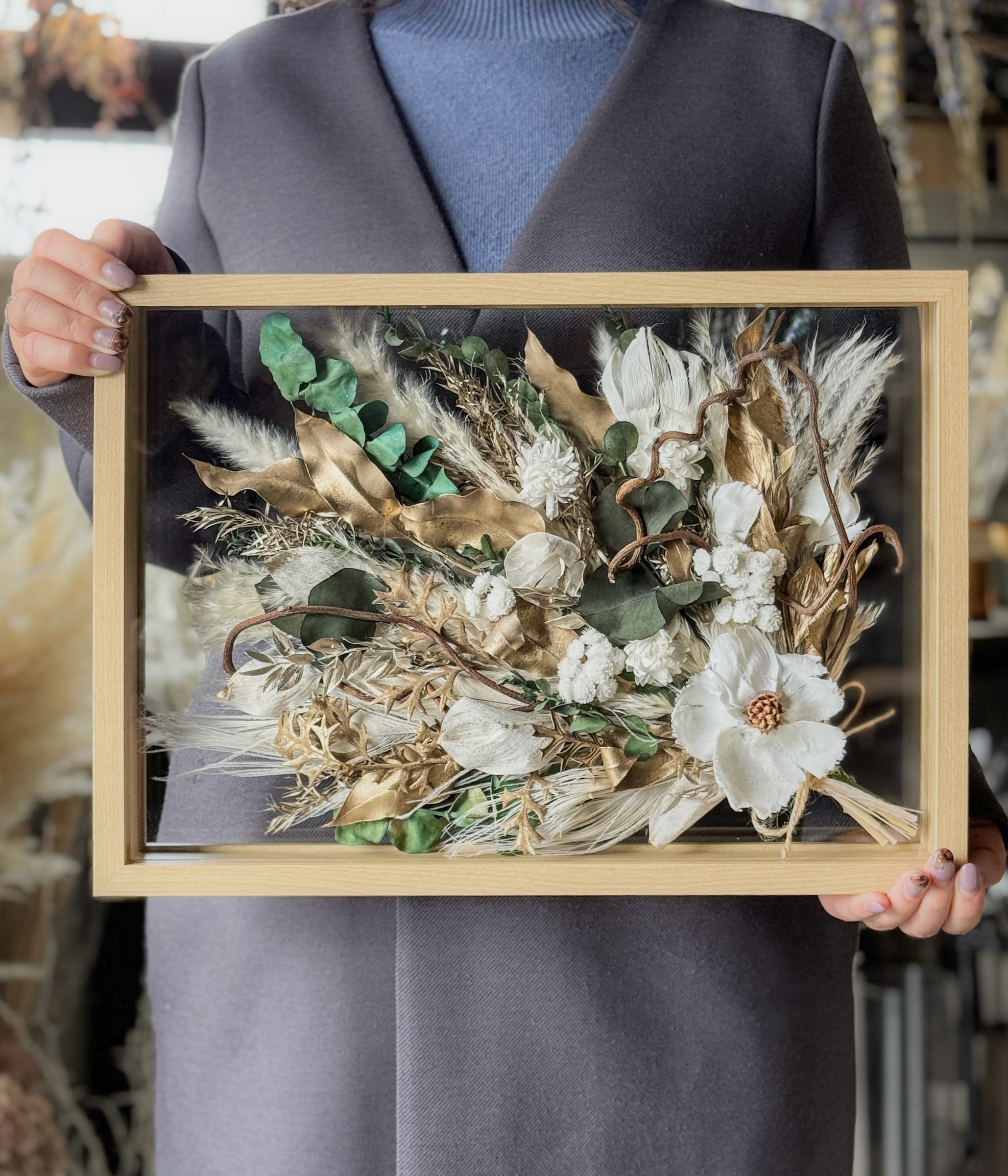 白と金の花材をおさめたフレームアレンジを手にしたところ